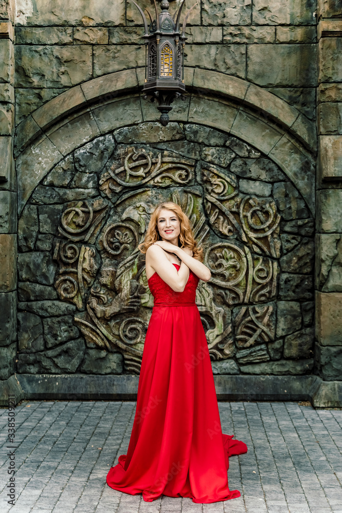 A woman in a red dress stands on a background of a medieval castle