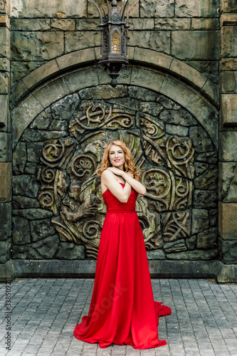 A woman in a red dress stands on a background of a medieval castle