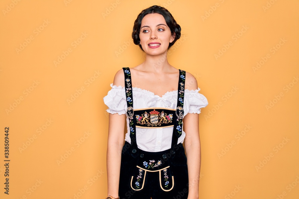 Young beautiful german woman with blue eyes wearing traditional octoberfest dress looking away to side with smile on face, natural expression. Laughing confident. Young beautiful german woman with blue eyes wearing traditional octoberfest dress looking away to side with smile on face, natural expression. Laughing confident.
