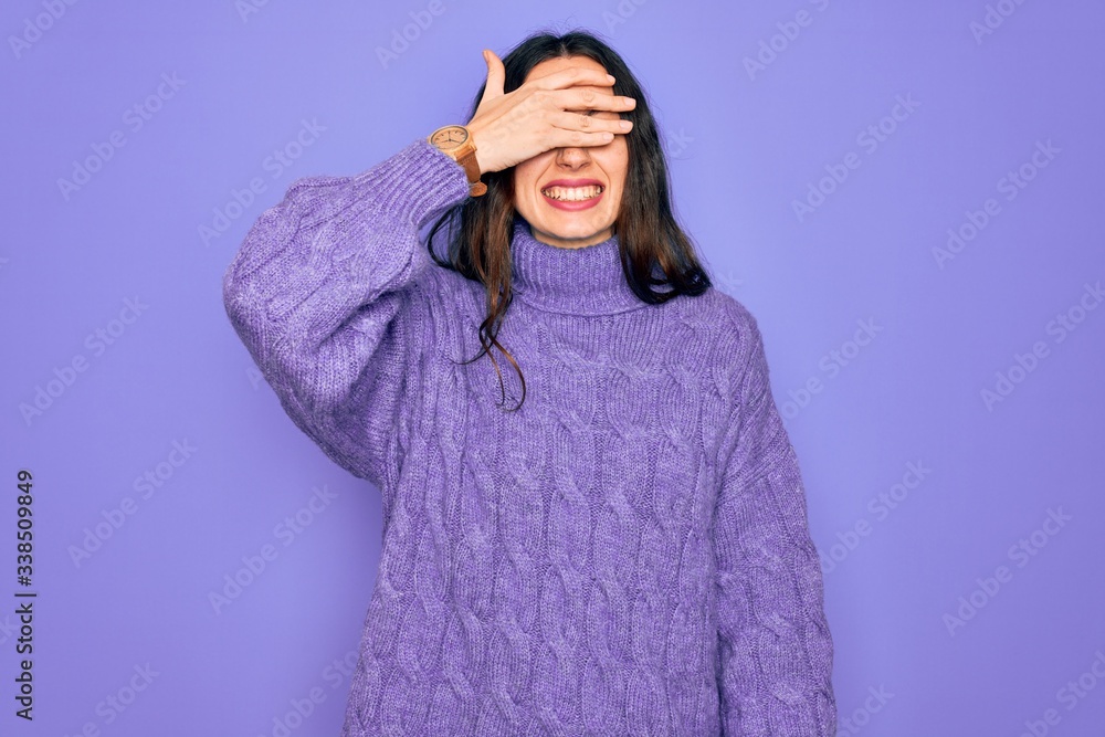 Young beautiful woman wearing casual turtleneck sweater standing over purple background smiling and laughing with hand on face covering eyes for surprise. Blind concept. Young beautiful woman wearing casual turtleneck sweater standing over purple background smiling and laughing with hand on face covering eyes for surprise. Blind concept.