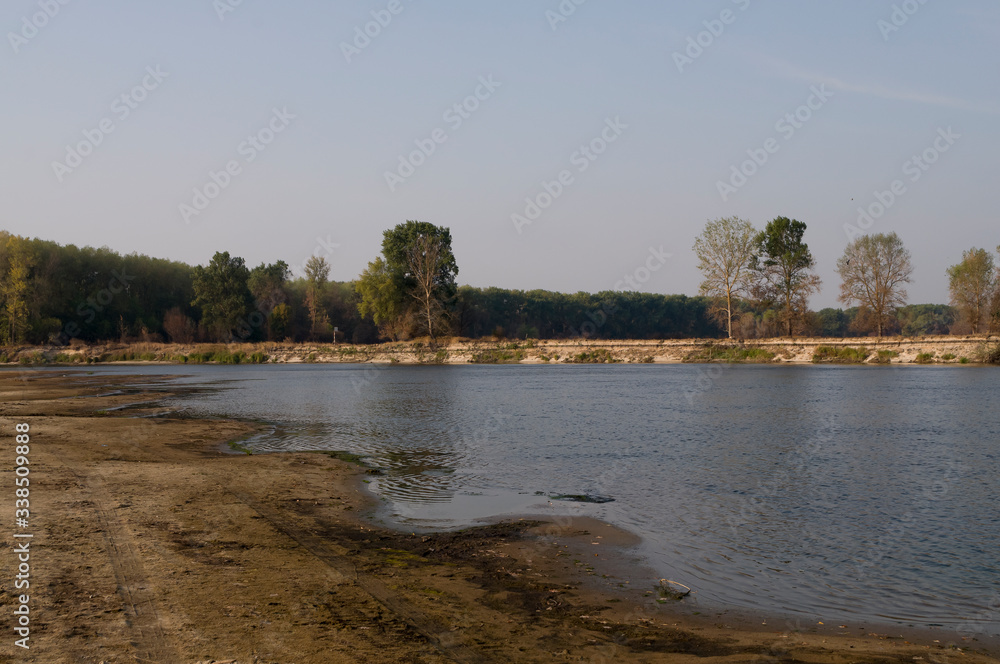 Blue river slow flowing across the green meadow and yellow sand with reflections of  trees in the water.  Fall