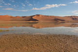 After the storm, the dunes are reflected in the water for a short time until the hot sun begans to dry the land, cracking it. Sossusvlei, Namib-Naukluft National Park, Namib desert, Namibia.