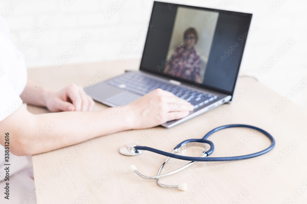 Fototapeta premium gp hosts an online appointment with an elderly quarantined patient at home. Female doctor at the desk talking to an elderly woman on a web camera and gives treatment recommendations