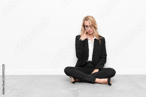 young blonde woman keeping an eye on you, not trusting, watching and staying alert and vigilant sitting on the floor
