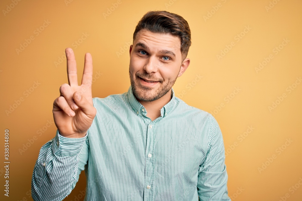 Young business man with blue eyes wearing elegant green shirt over yellow background showing and pointing up with fingers number two while smiling confident and happy. Young business man with blue eyes wearing elegant green shirt over yellow background showing and pointing up with fingers number two while smiling confident and happy.