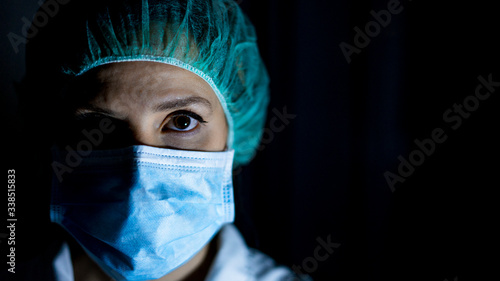 Portrait of young female surgeon, wearing mask and a surgical mask, in front of black background