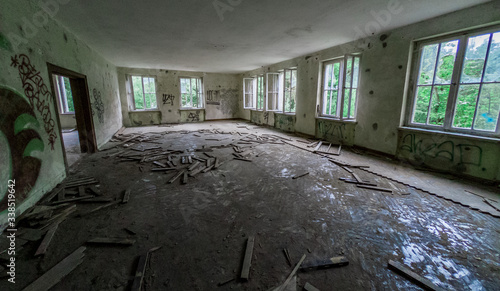 An abandoned room with broken windows an trees outside the derelict building