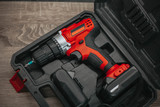 red electric drill lies in a dark suitcase on a wooden table