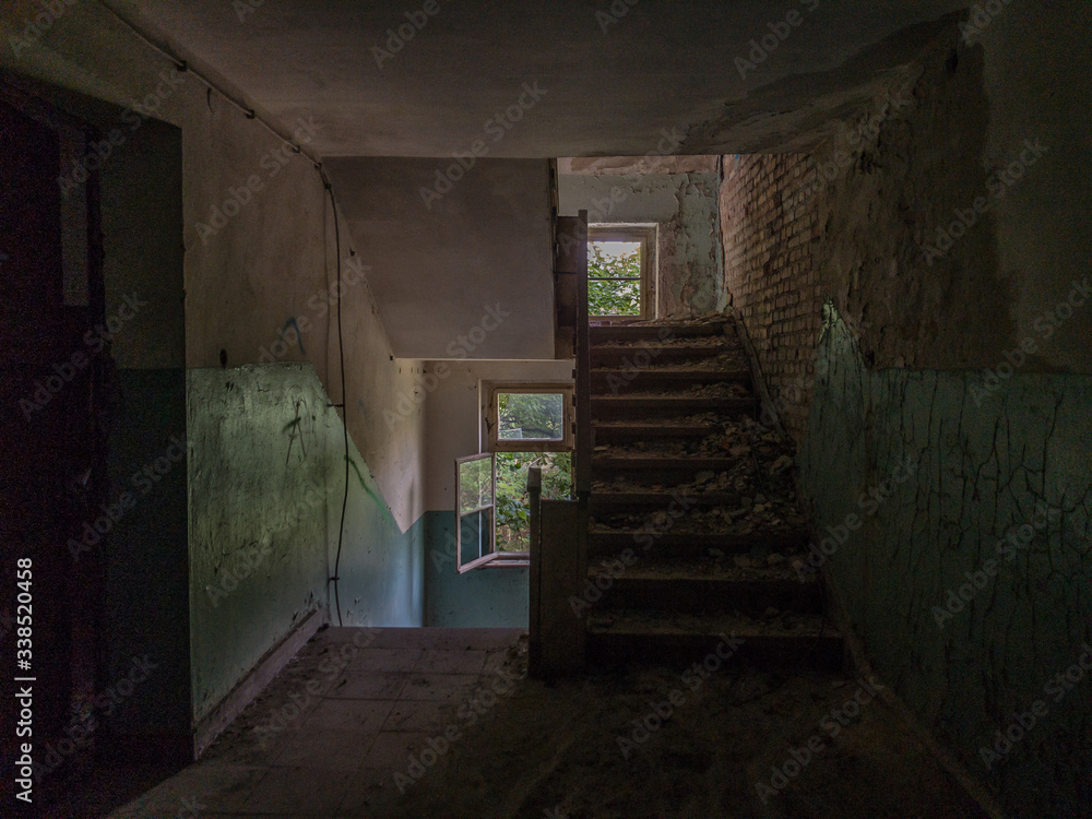A derelict staircase in an abandoned house, gloomy lighting and a forest seen through the windows