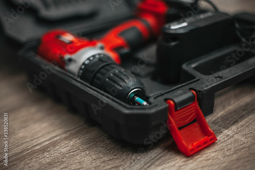 red electric drill lies in a dark suitcase on a wooden table