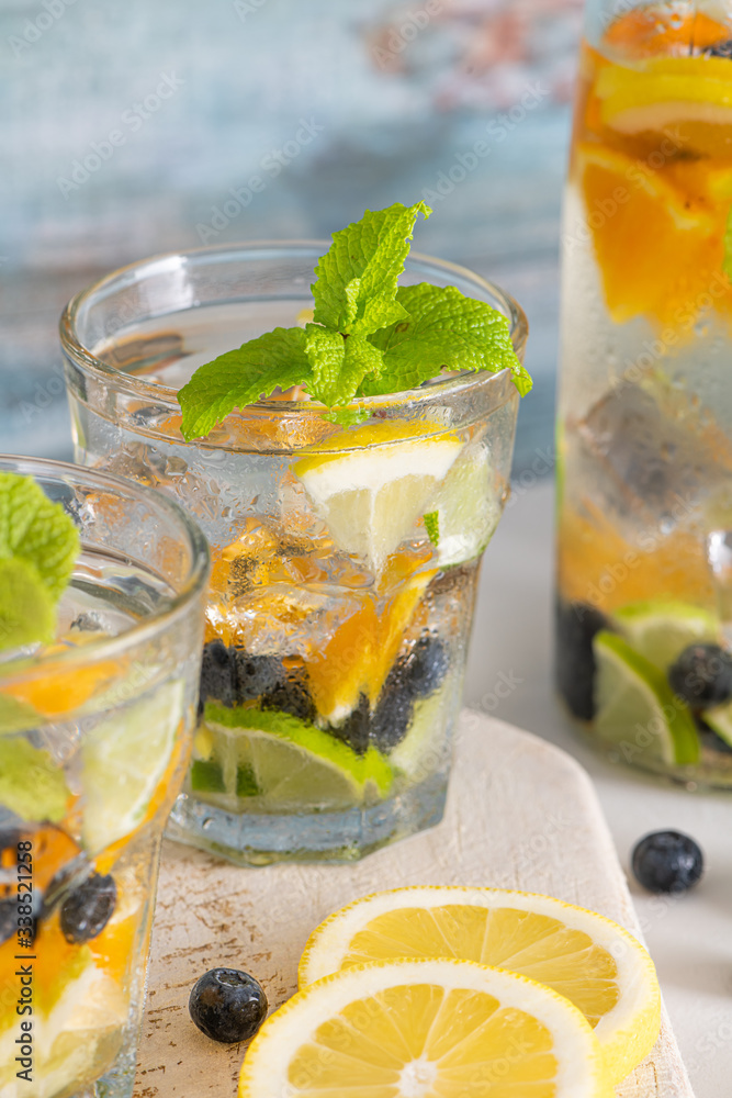 Summer healthy cocktails of citrus infused waters, lemonades or mojitos, with lime lemon orange blueberries and mint, diet detox beverages, in glasses on light background