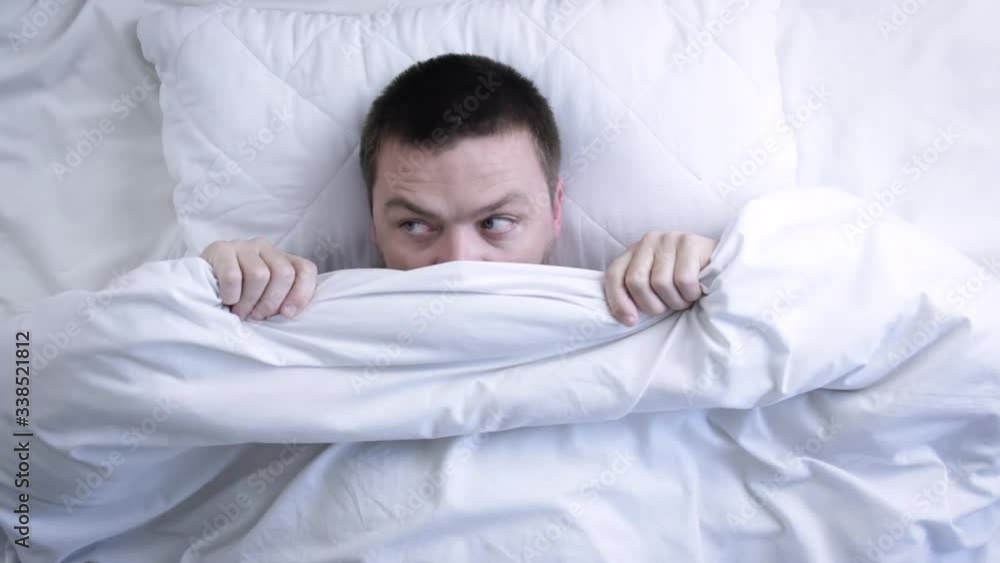 Young scared man hiding in bed under the blanket at home. Nightmare concept Young scared man hiding in bed under the blanket at home. Nightmare concept
