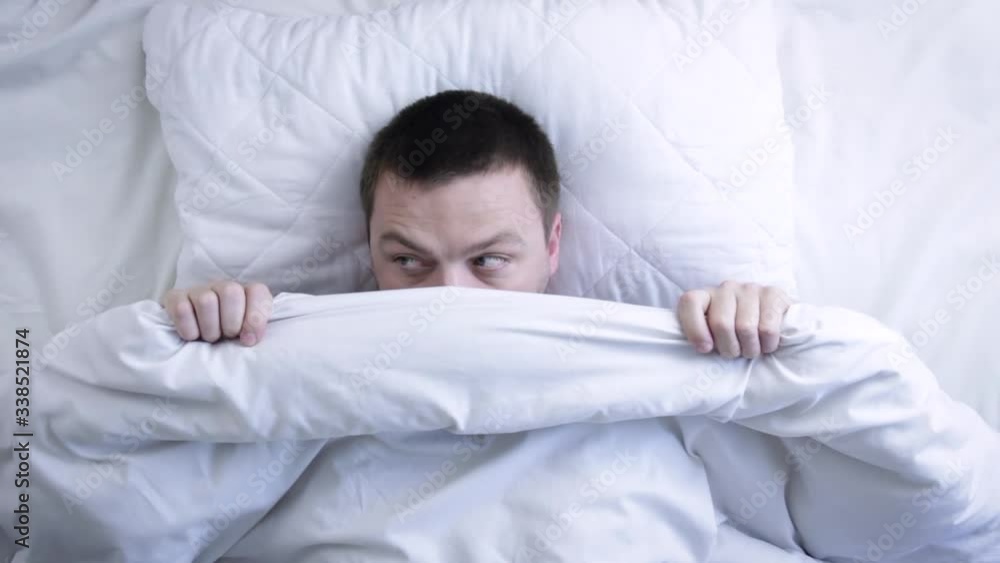 Young scared man hiding in bed under the blanket at home. Nightmare concept Young scared man hiding in bed under the blanket at home. Nightmare concept
