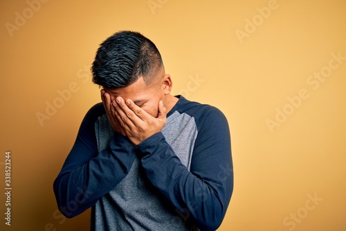 Young handsome latin man wearing casual t-shirt standing over yellow background with sad expression covering face with hands while crying. Depression concept. © Krakenimages.com