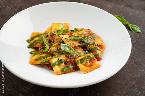 Cooked ravioli with tomatoes, pesto sauce and Basil leaves on a white plate, close-up