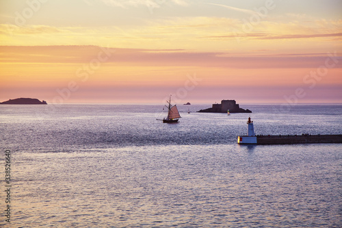 An old sailboat enters the Bay of Saint Malo at sunset. France. Brittany