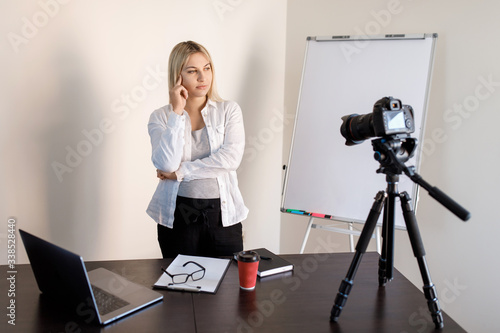 Online education, educational blogging. A young pregnant woman tutor records training video lessons to the camera, she stands and shows with a pen on a flip chart with graphs and diagrams