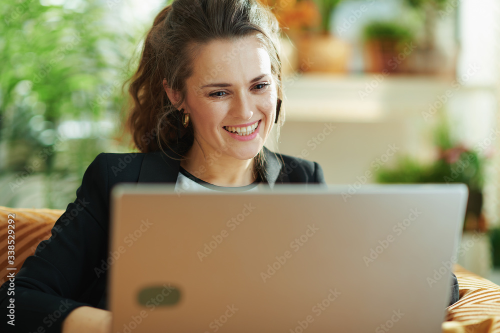 happy trendy woman using laptop while sitting on sofa
