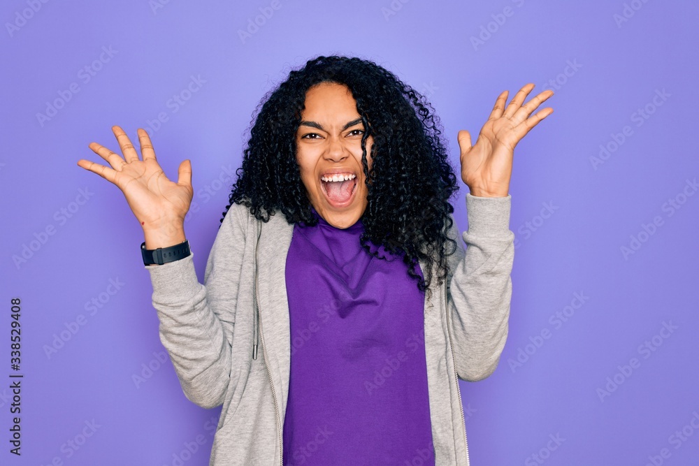 Young african american sporty woman wearing casual sweatshirt over purple background celebrating crazy and amazed for success with arms raised and open eyes screaming excited. Winner concept Young african american sporty woman wearing casual sweatshirt over purple background celebrating crazy and amazed for success with arms raised and open eyes screaming excited. Winner concept