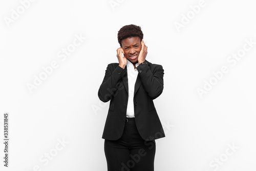 young pretty black womanlooking angry, stressed and annoyed, covering both ears to a deafening noise, sound or loud music against white wall photo