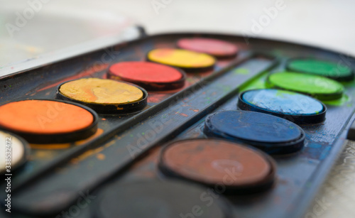 Colors on watercolor palette closeup. Selective focus. Black, blue, brown, red, yellow, green, orange colors on palette. 