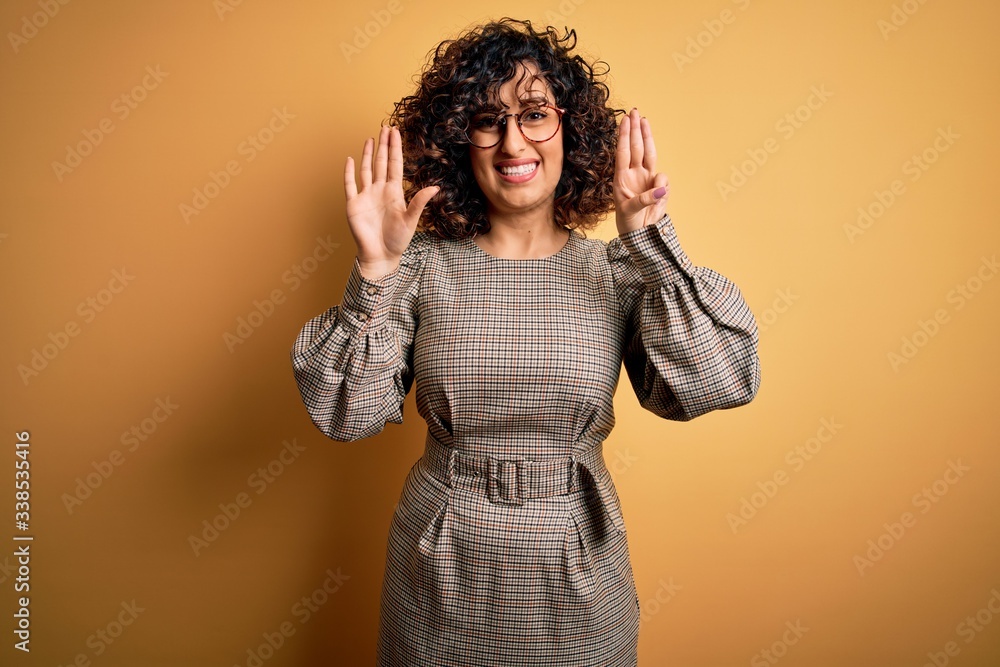 Beautiful arab business woman wearing dress and glasses standing over yellow background showing and pointing up with fingers number eight while smiling confident and happy. Beautiful arab business woman wearing dress and glasses standing over yellow background showing and pointing up with fingers number eight while smiling confident and happy.