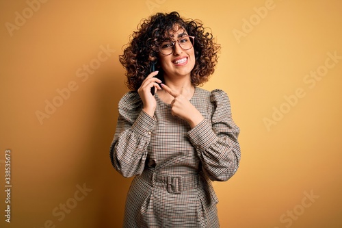 Beautiful arab businesswoman wearing glasses having conversation talking on smartphone very happy pointing with hand and finger © Krakenimages.com