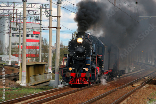 Retro steam train in clouds of smoke riding along the railway rolling tourists