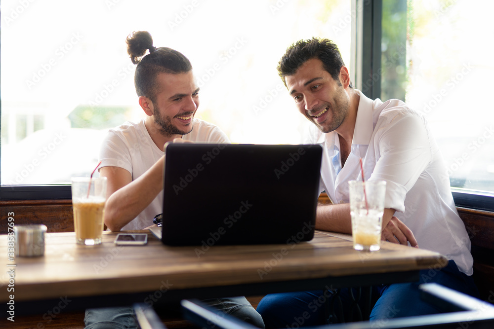 Two happy men as friends using laptop together at the coffee shop