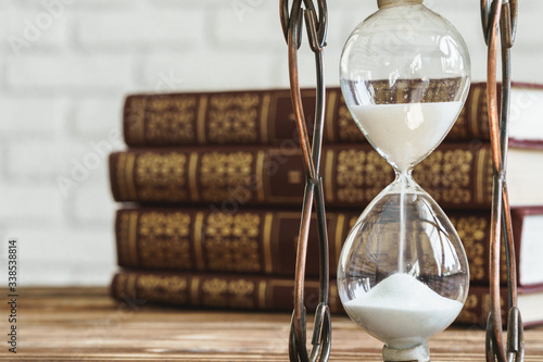 Vintage hourglass against a stack of old books close up