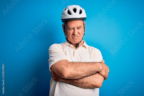 Middle age hoary cyclist man wearing bike security helmet over isolated blue background skeptic and nervous, disapproving expression on face with crossed arms. Negative person.
