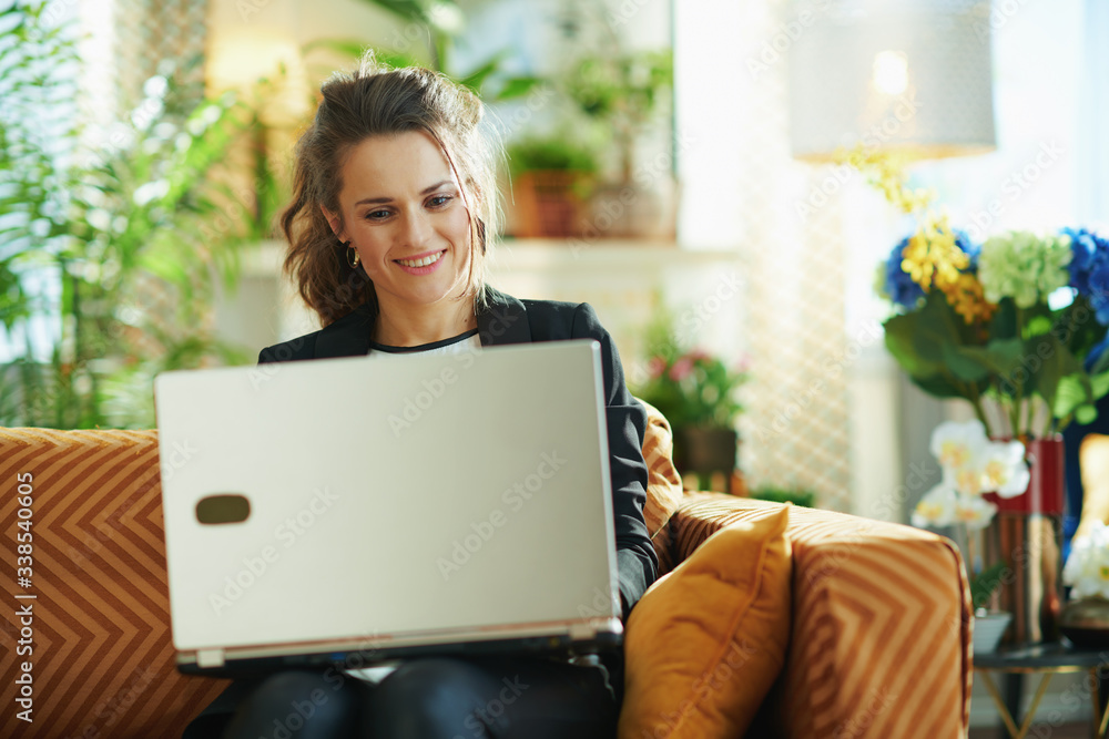 Naklejka premium smiling elegant middle age woman with laptop sitting on couch