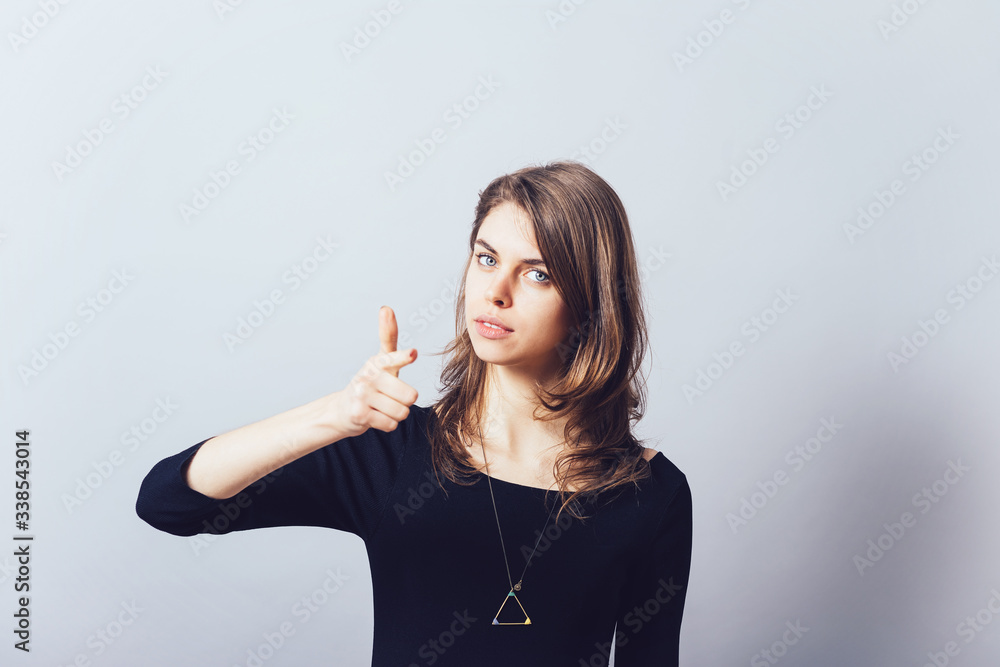 Woman index finger at the camera forward. On a gray background. Woman index finger at the camera forward. On a gray background.