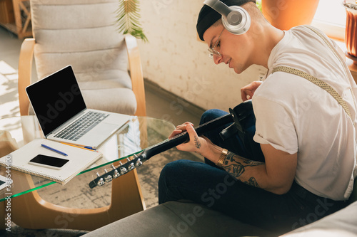 Man studying at home during online courses or free information by hisself. Becomes musician  guitarist while isolated  quarantine against coronavirus spreading. Using laptop  smartphone  headphones.