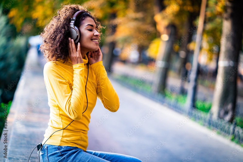 Φωτογραφία African teenager girl listens to music with headphones in park