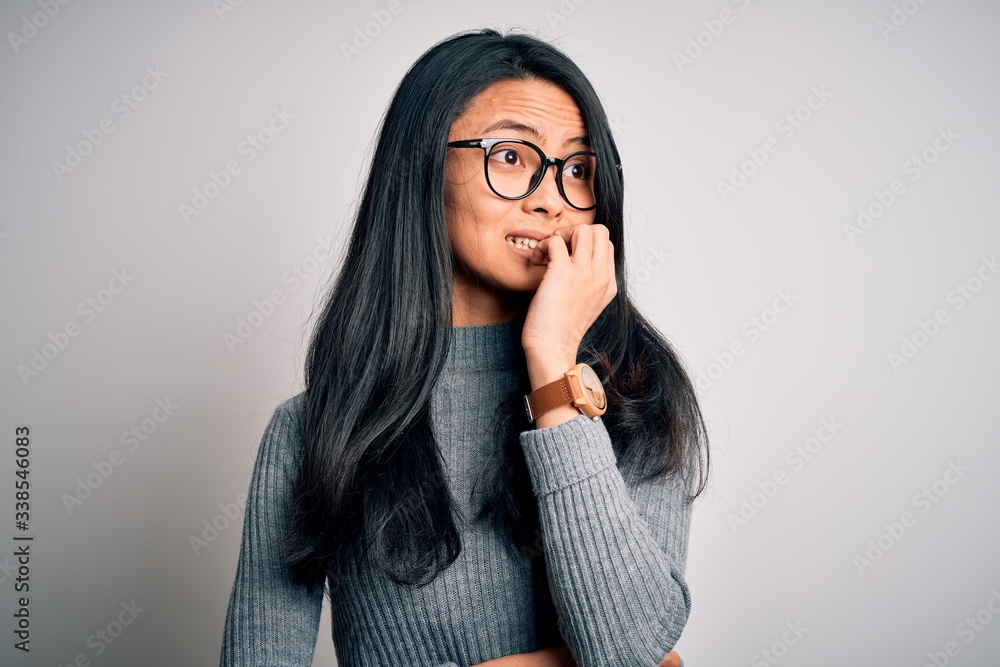 Young beautiful chinese woman wearing glasses and sweater over isolated white background looking stressed and nervous with hands on mouth biting nails. Anxiety problem. Young beautiful chinese woman wearing glasses and sweater over isolated white background looking stressed and nervous with hands on mouth biting nails. Anxiety problem.