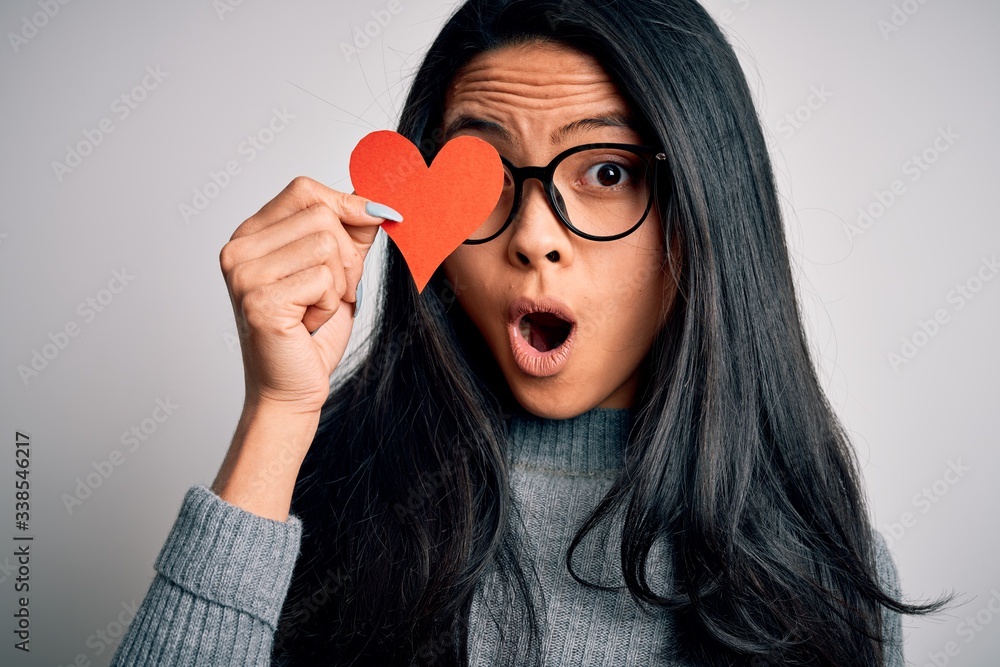Young beautiful chinese woman holding paper heart over isolated white background scared in shock with a surprise face, afraid and excited with fear expression Young beautiful chinese woman holding paper heart over isolated white background scared in shock with a surprise face, afraid and excited with fear expression