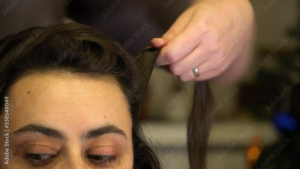 The stylist works with strands of the girl's hair using a comb and hairspray The stylist works with strands of the girl's hair using a comb and hairspray