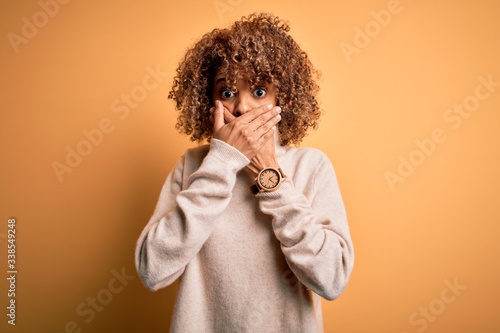 Young beautiful african american woman wearing turtleneck sweater over yellow background shocked covering mouth with hands for mistake. Secret concept.