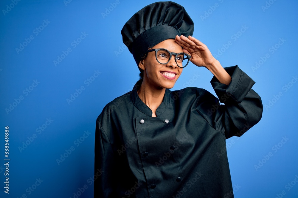 Young african american chef woman wearing cooker uniform and hat over blue background very happy and smiling looking far away with hand over head. Searching concept. Young african american chef woman wearing cooker uniform and hat over blue background very happy and smiling looking far away with hand over head. Searching concept.