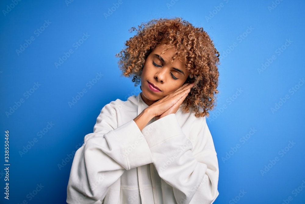 Beautiful african american sporty woman wearing casual sweatshirt over blue background sleeping tired dreaming and posing with hands together while smiling with closed eyes. Beautiful african american sporty woman wearing casual sweatshirt over blue background sleeping tired dreaming and posing with hands together while smiling with closed eyes.