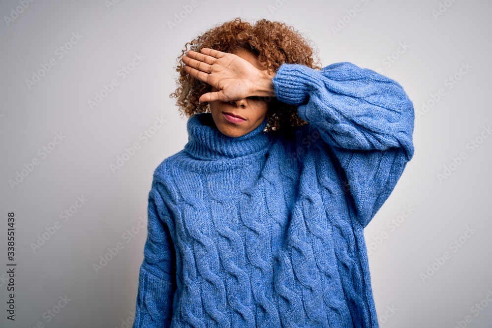 Obraz premium Young beautiful african american woman wearing turtleneck sweater over white background covering eyes with arm, looking serious and sad. Sightless, hiding and rejection concept