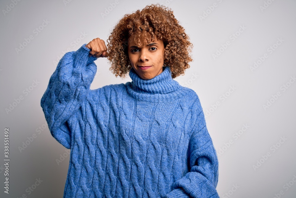 Young beautiful african american woman wearing turtleneck sweater over white background Strong person showing arm muscle, confident and proud of power Young beautiful african american woman wearing turtleneck sweater over white background Strong person showing arm muscle, confident and proud of power