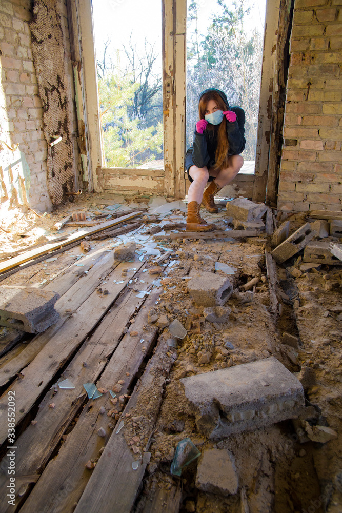 Girl in a sweatshirt and brown boots is sittig in an abandoned building in a blue medical mask and pink gloves. Coronavirus. COVID-19 Girl in a sweatshirt and brown boots is sittig in an abandoned building in a blue medical mask and pink gloves. Coronavirus. COVID-19