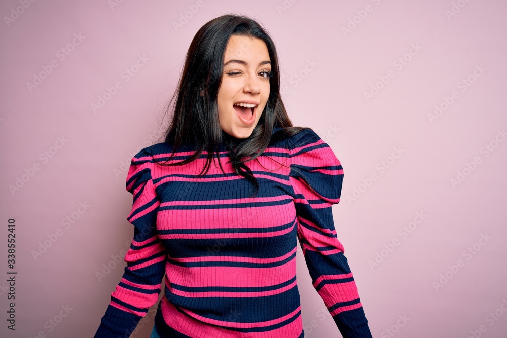 Young brunette elegant woman wearing striped shirt over pink isolated background winking looking at the camera with sexy expression, cheerful and happy face. Young brunette elegant woman wearing striped shirt over pink isolated background winking looking at the camera with sexy expression, cheerful and happy face.