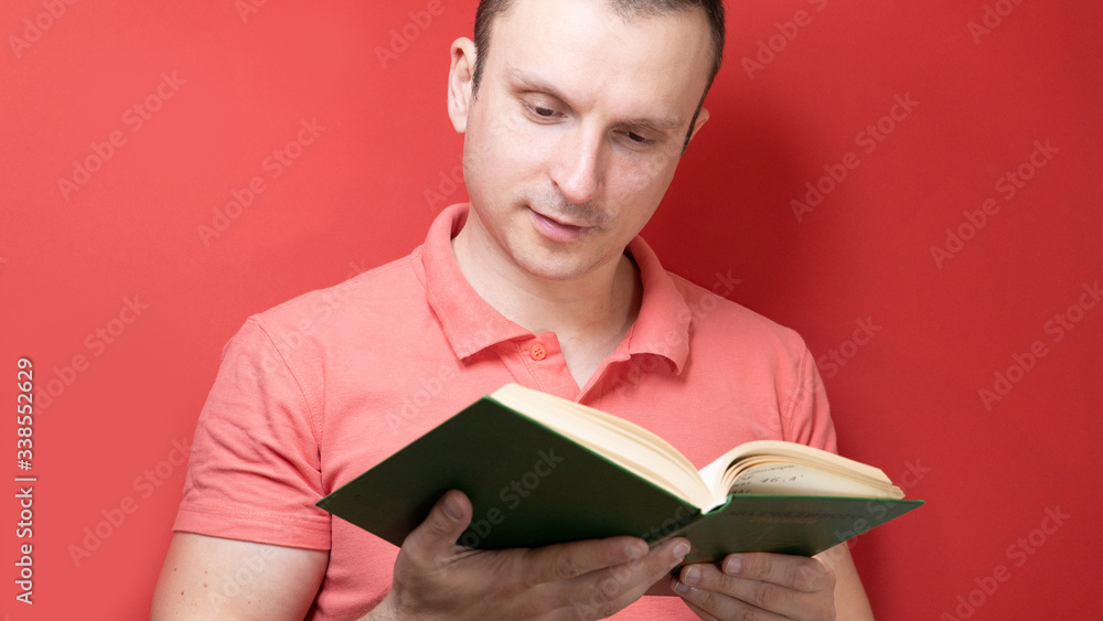 A smiling young stylish student stands with books on a clear red background in a casual bright Polo, pointing to the copy space A smiling young stylish student stands with books on a clear red background in a casual bright Polo, pointing to the copy space