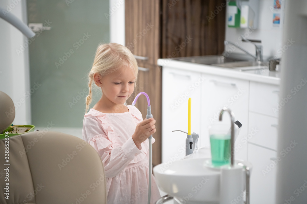 A little blond girl in the dental clinic. A cup with sterile water for rinsing the mouth in the foreground. A visit to a dentist concept