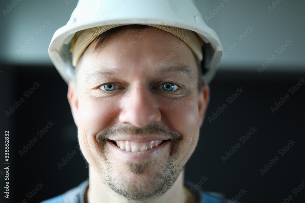 Close-up of cheerful worker face. Macro shot of foreman in protective white helmet posing on camera indoors. Happy handyman. Renovation and interior designer concept Close-up of cheerful worker face. Macro shot of foreman in protective white helmet posing on camera indoors. Happy handyman. Renovation and interior designer concept