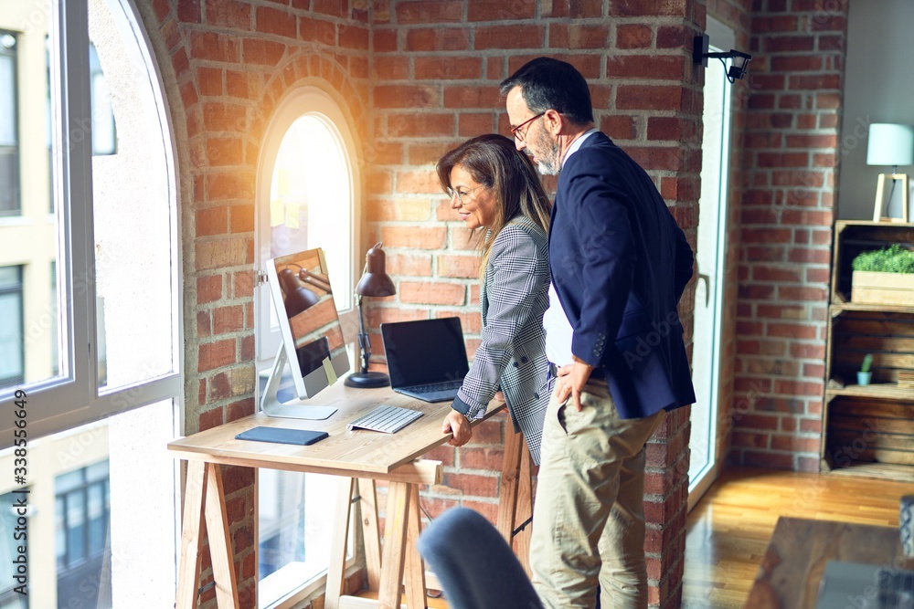 Two middle age business workers smiling happy and confident. Standing with smile on face working together using laptop at the office Two middle age business workers smiling happy and confident. Standing with smile on face working together using laptop at the office