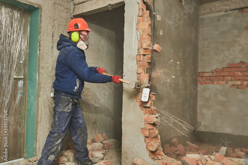 demolition work and rearrangement. worker with sledgehammer destroying wall photo